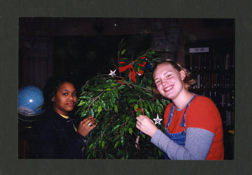 Scripps students smile next to a festively decorated Christmas tree, Scripps College