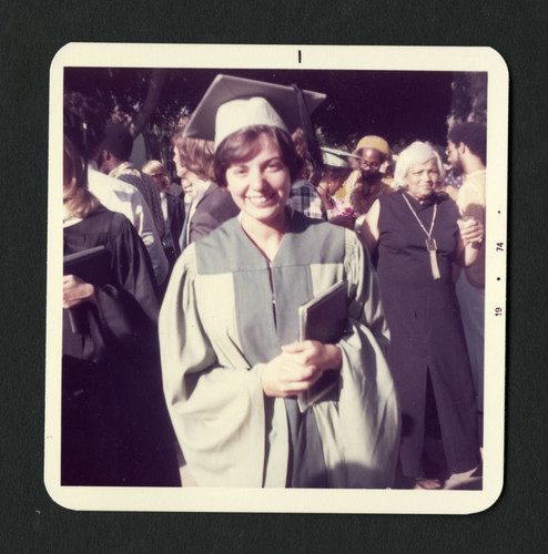 Scripps student wearing a green graduation gown and cap proudly holds her diploma, Scripps College