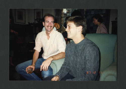 Two male colleagues smile at eachother at Denison Library's Christmas tea, Scripps College