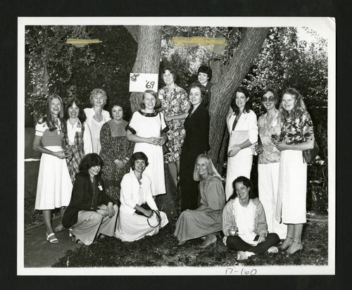 Scripps alumnae standing by a class of '69 sign nailed to a tree in Margaret Fowler Garden, Scripps College