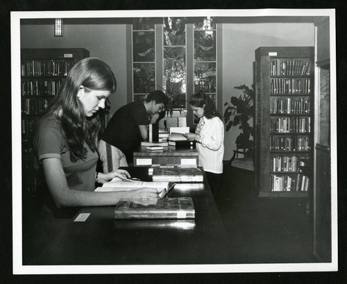 Three students reading books on top of bookcases in Denison Library, Scripps College