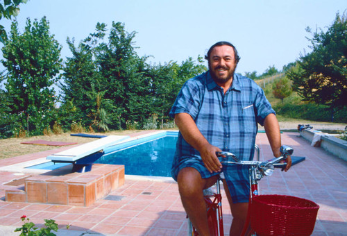 Luciano Pavarotti on red bicycle near pool