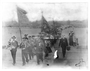 Sailors and citizens walking down a pier in Los Angeles, bearing flowers