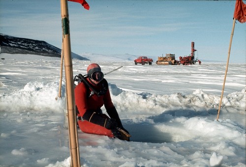 Diver at drilled hole through the sea ice in order to access the ocean below. Ice driller in background. McMurdo Station, Antarctica [Drill 8]