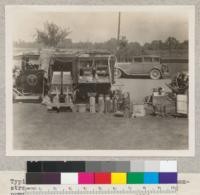 Typical set-up for rural fire protection demonstration, 1930. Fire extinguishers and back pumps on the ground. Hand tools on top of truck. Electrical hazards in case on top