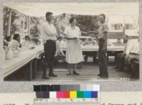 The chief of the tribe of Crows cut the cake won in the tribal contests. Mrs. Milnes - cook - holds it while Farm Advisor Garthwaite (left) and Camp manager Small (right) look on with interest