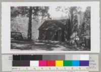 Caretaker Charles Crose and J. W. Floyd in front of Live Oak Lodge, Whitaker's Forest, beside one of the large second-growth sequoia trees. Tree at left is an incense cedar. Metcalf