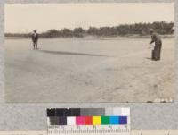 Fairbanks demonstrating stream thrown by double-acting pump in five gallon pump extinguisher. Black spot on ground indicates distance to which water is thrown