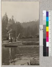 Second Growth Redwood Cutting Experiment, Project #688, Big River, Mendocino County, California. View showing how second growth logs are pulled from the cars to the roll-way. The stern wheel river barge is equipped with a drum which was pressed into this service. This barge is used for towing rafts of logs from the dump to the mill and for bringing back heavy supplies. E. Fritz, May 1923