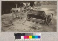 Sand spreader and tree packer invented by D. S. Olson. Sand is loaded into hopper and feeds forward onto bed from canvas sheet. Wheels can move separately by simple differential. Two men haul the spreader over the bed. It covers as smoothly as a sidewalk
