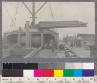 Loading lumber on boat Katherine. Man operating double winch on prow of boat. Large ropes placed around packets of lumber which are lifted bodily in the air and deposited in the hold of the boat. Only green lumber and rough stock is shipped this way. Finished stock, mouldings pipe stock, etc., now shipped by train over Northwestern Pacific Railroad. Bayside Lumber Company, Humboldt County