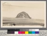 Morro Rock from shore in village of Morro, San Luis Obispo County, California. This treeless barren knoll sticks up out of the ocean about a mile off shore and with its projecting sand spit offers shelter to small boats at high tide. The Hayne plantation of eucalyptus is directly south of this rock. 1916