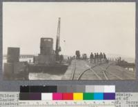 Tilden Lumber Company, foot of University Avenue, Berkeley. Lumber float barge of Coos Bay Lumber Company, in act of discharge of last of cargo on to trucks on the wharf. Barge has its derrick. Forestry 112 class on dock. Oct., 1920. E.F