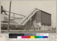 Forestry 112 on a visit to the Standard Oil Company's box factory. The picture shows the large bin and its elevator for handling mill blocks. Note the construction-concrete below and 2 x 6's lying flat for the wall above; also the delivery chutes and the gondola car loaded with blocks. Oct. 1925. E.F