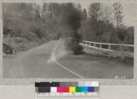 A motorcycle burning up on the highway near Placerville, April 1933. Might be cause of a bad forest fire in summer time unless highway was cleaned up. Metcalf