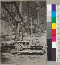 Peeling redwood at the landing. Casper Lumber Company, Camp 20. Bulldozer has just rolled a log to the loading boom which has gripped the log with tongs and is ready to raise it for loading. 8/20/40. E.F