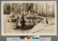 Loading sleigh with cross haul. Although the loaders moved, you can see the location of the send up men on the ground and the manner in which they are using their cant hooks to guide the log up straight and the top loader on top the load. At the left can be seen the loading chain as it is pulled taut by the cross haul team