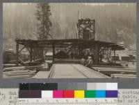 End of tramway, unloading the lumber on to a sorting table. A package shown just as it was dropped on to table. Tramway can be seen (also 2 loads lumber en route) on slope behind the housing. Spanish Peak Lumber Company, Quincy, California. August, 1920. E.F