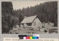 Whitaker's Forest headquarters cabin with the camp-fire circle in the foreground. The boys' camp is in the timber just above the old fallen tree stump. Metcalf. July, 1928. Lantern slide made