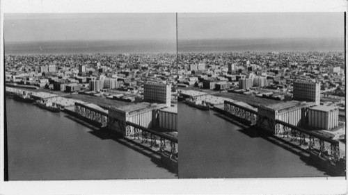 Airview of City of Galveston, Texas. Picture is taken looking from docks on Galveston Bay across Galveston Island to the Gulf of Mexico in background. In foreground are grain elevators of Galveston wharves, principal origin of greatest gulf grain export cargoes. 6/24/48 Copy supplies by Galveston Chamber of Commerce. Original print ret'd to owner 8/6/48
