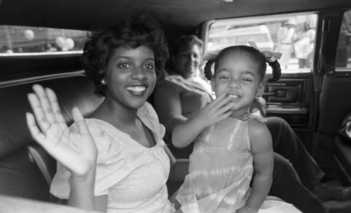 Woman and little girl waving from the backseat of a car during a parade, Los Angeles, 1982