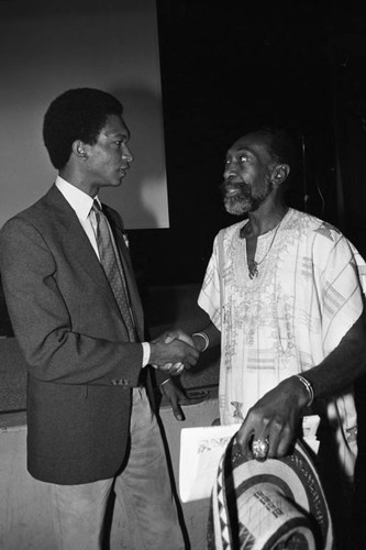 Two African American men greeting each other in front of a stage, Los Angeles, 1983