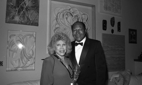 Tom Bradley posing with a woman during a formal event at a private home, Los Angeles, 1990