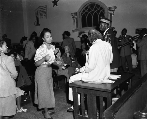 Bishop Charles Manuel "Sweet Daddy" Grace talking with a woman during a worship service, Los Angeles, ca. 1950