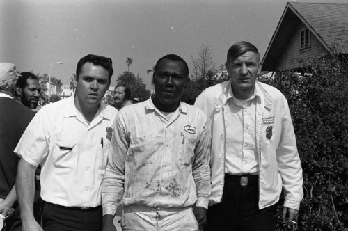 First responders standing with a victim of a sewer explosion and flash fire, Los Angeles, 1972