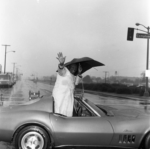 Unidentified man waving from a Corvette, Compton, 1973