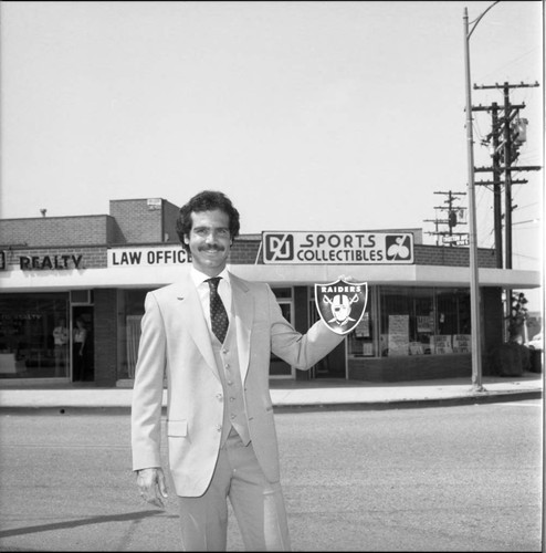 Man holding a Raider's emblem in front of DJ Sports Collectibles, Los Angeles, 1985