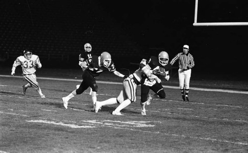 Crenshaw and Carson High School football teams running a play during a city championship game, Los Angeles, 1982