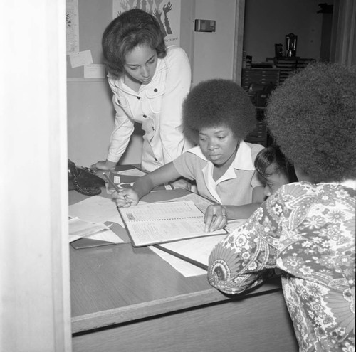 Compton College students examining a planner or scheduling book, Los Angeles, ca. 1972