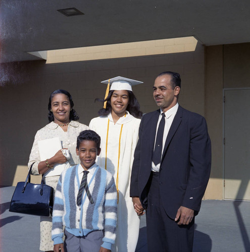 Young woman wearing a graduation gown posing with her family, ca. 1968