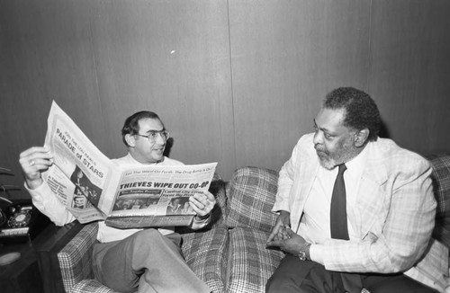 James Cleaver and an unidentified man with a newspaper sitting on a couch, Los Angeles, 1983