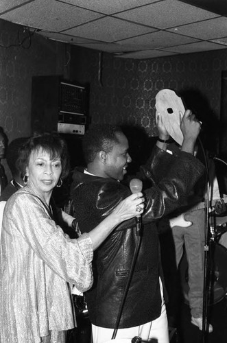 Gertrude Gipson holding a microphone for Freddie Jackson at the Pied Piper nightclub, Los Angeles, 1985