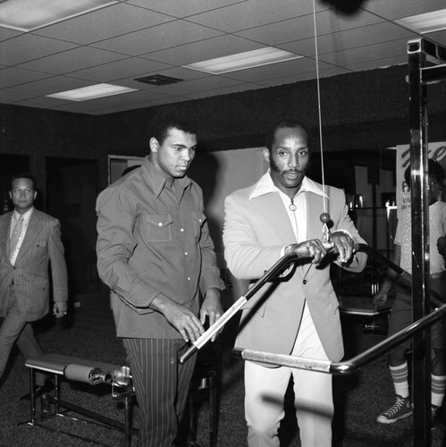 Muhammad Ali listening to instructions from Earl Maynard at a fitness center, Compton, 1973