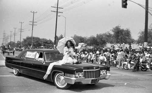 Woman riding in a parade with a parasol during the Watts Summer Festival, Los Angeles, ca. 1973