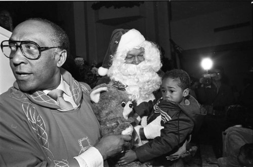 Rev. H.H. Brookins with Tom Bradley in a Santa suit talking to a child, Los Angeles, 1982