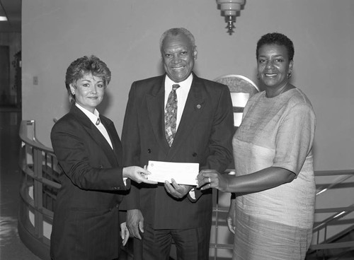 John W. Mack holding a check with two unidentified women, Los Angeles, 1991