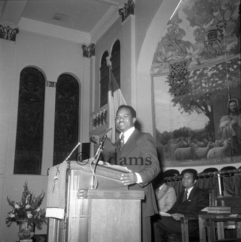 Judge Billy Mills listening to a man speaking from a pulpit, Los Angeles, 1975