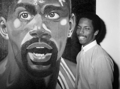 Artists Kevin Allen posing next to his painting of Magic Johnson, Los Angeles, 1984