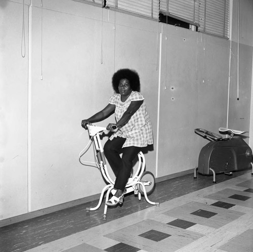 Woman working out on a exercise bike in the Compton College gym, Compton, 1972