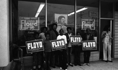 John Floyd posing with campaign supporters and their signs near a storefront, Los Angeles, 1974