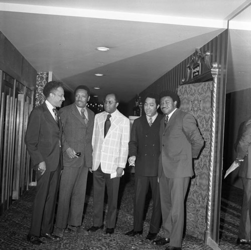 Men speaking together in a hallway at a press conference, Los Angeles, 1972