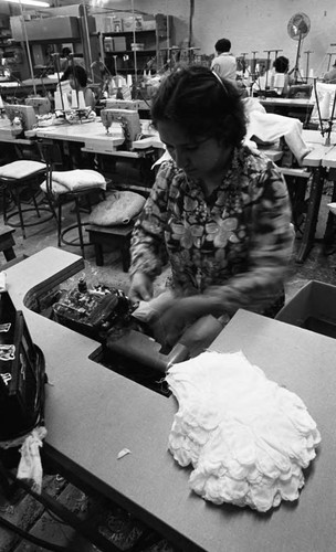 A woman sewing white gloves at her workstation in a workshop, Los Angeles, 1979