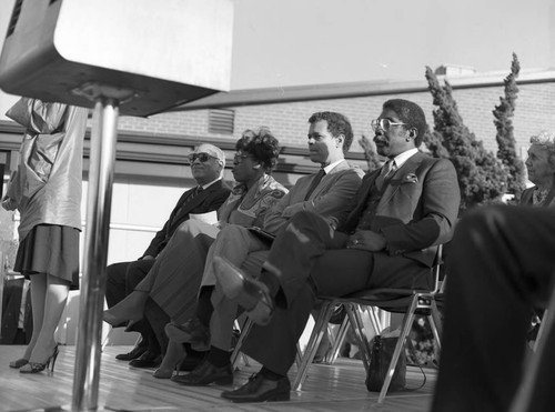 Julian Bond, Diane Watson and others sitting on an outdoor stage at Darby Park, Inglewood, 1985