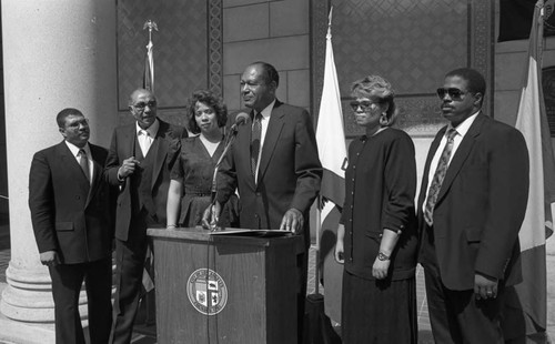 Tom Bradley speaking at lectern with the family of Jessie Mae Beavers, Los Angeles, 1989