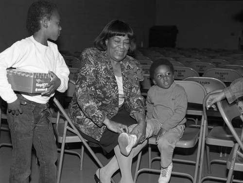 Woman tying a child's shoelace during a KangaROO shoe give-away, Los Angeles, 1985