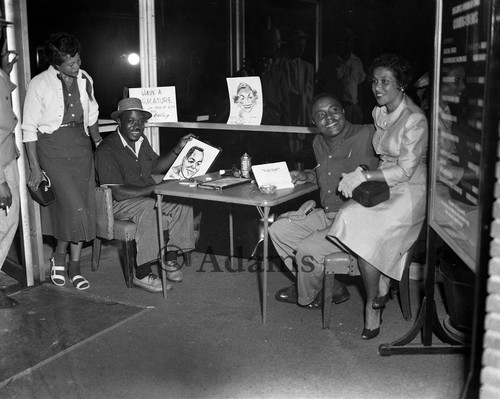 Cal Bailey sitting with subjects of his caricatures as he displays his work, Los Angeles, 1956